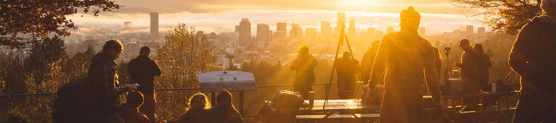 people silhouetted by sunset with city in background